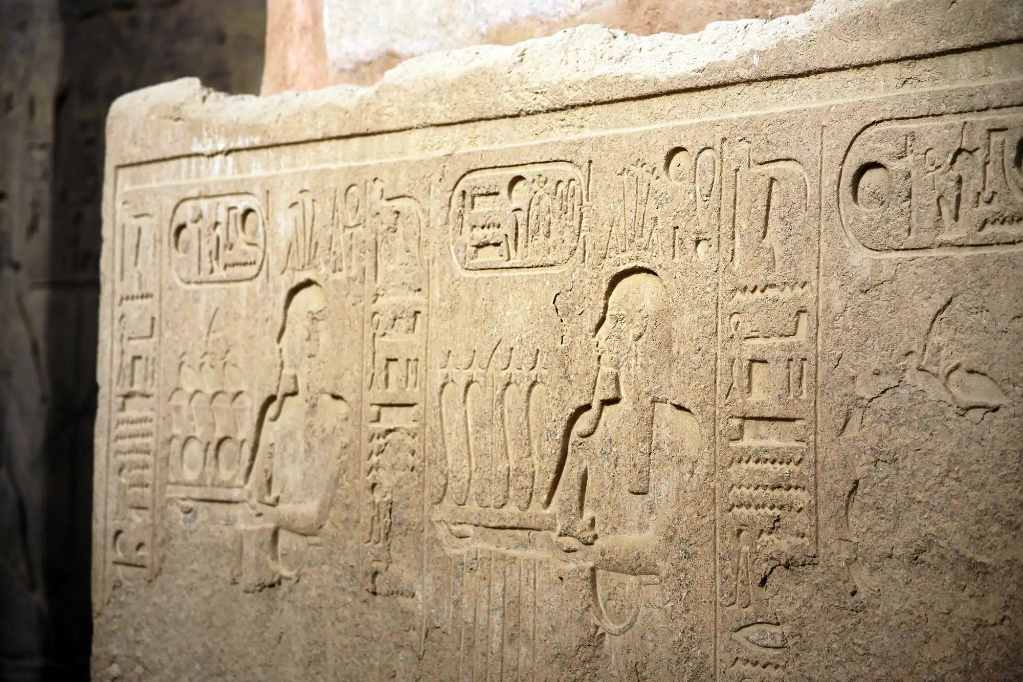 Close-up of carved figures on a sandstone block at Luxor Temple, edges worn soft and glowing in warm light.