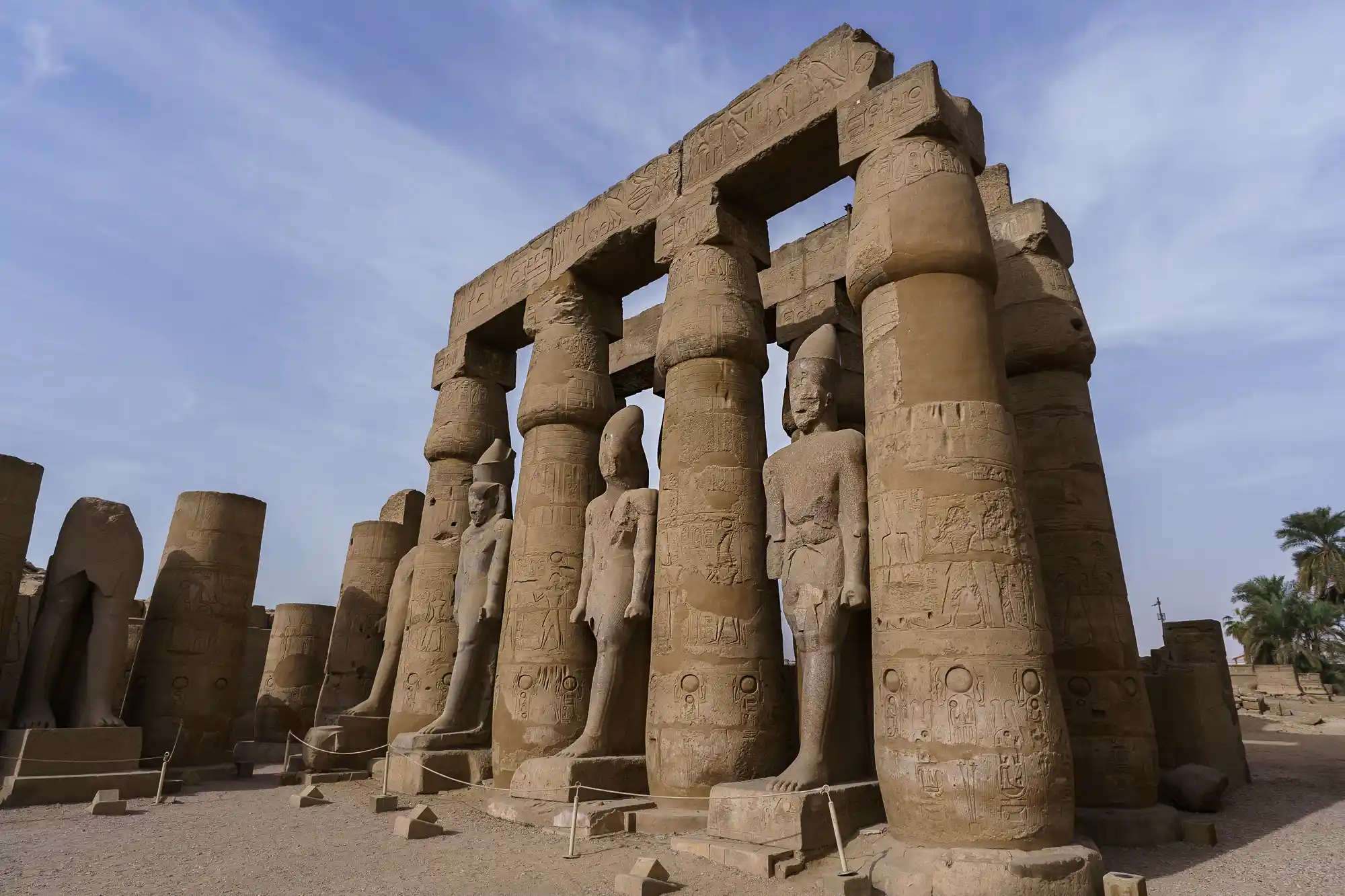 Sandstone columns carved with figures rise in bright overhead light inside Luxor Temple.
