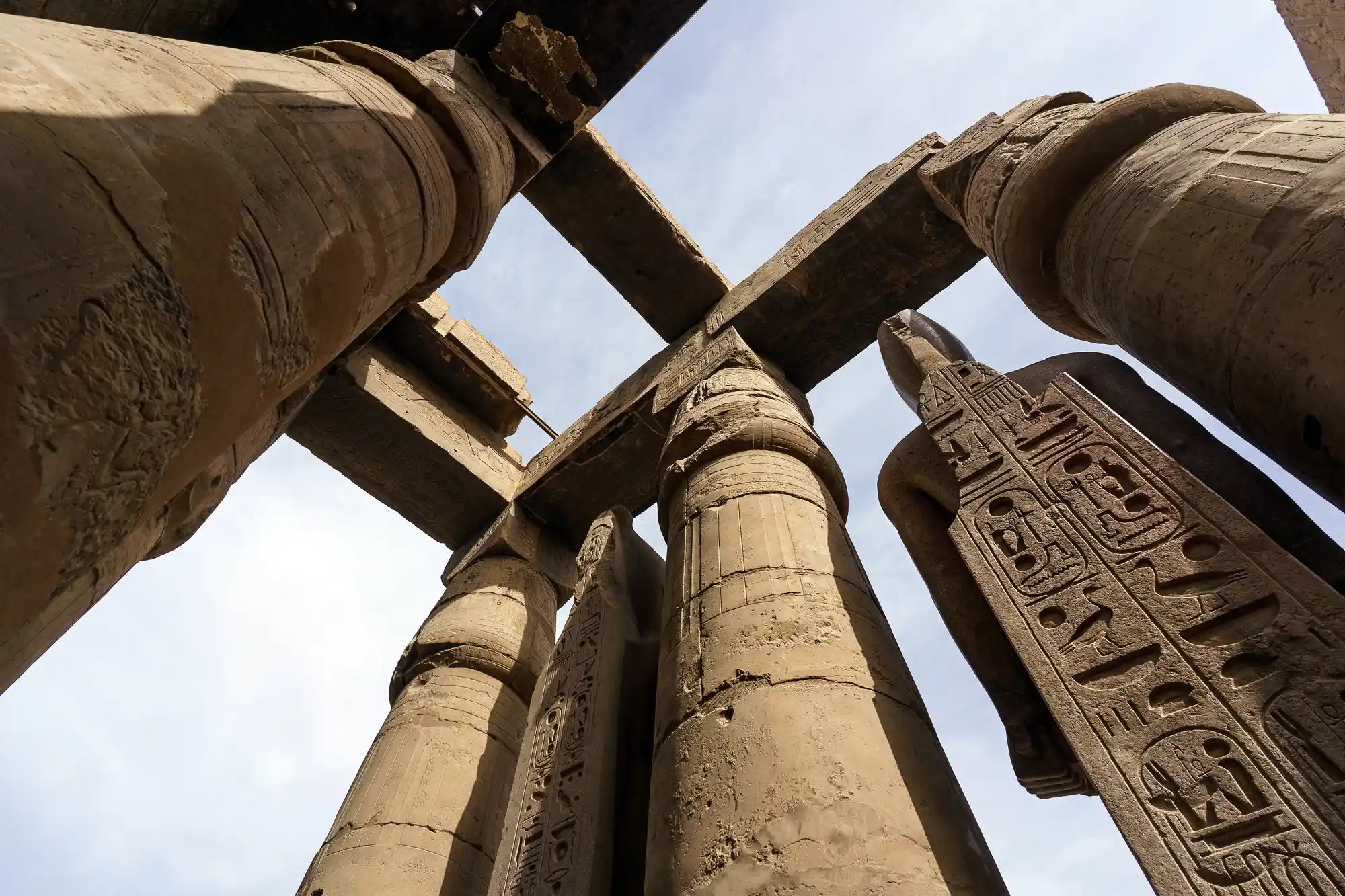 Looking up at the giant papyrus columns and carved stone beams of Luxor Temple under a pale sky.