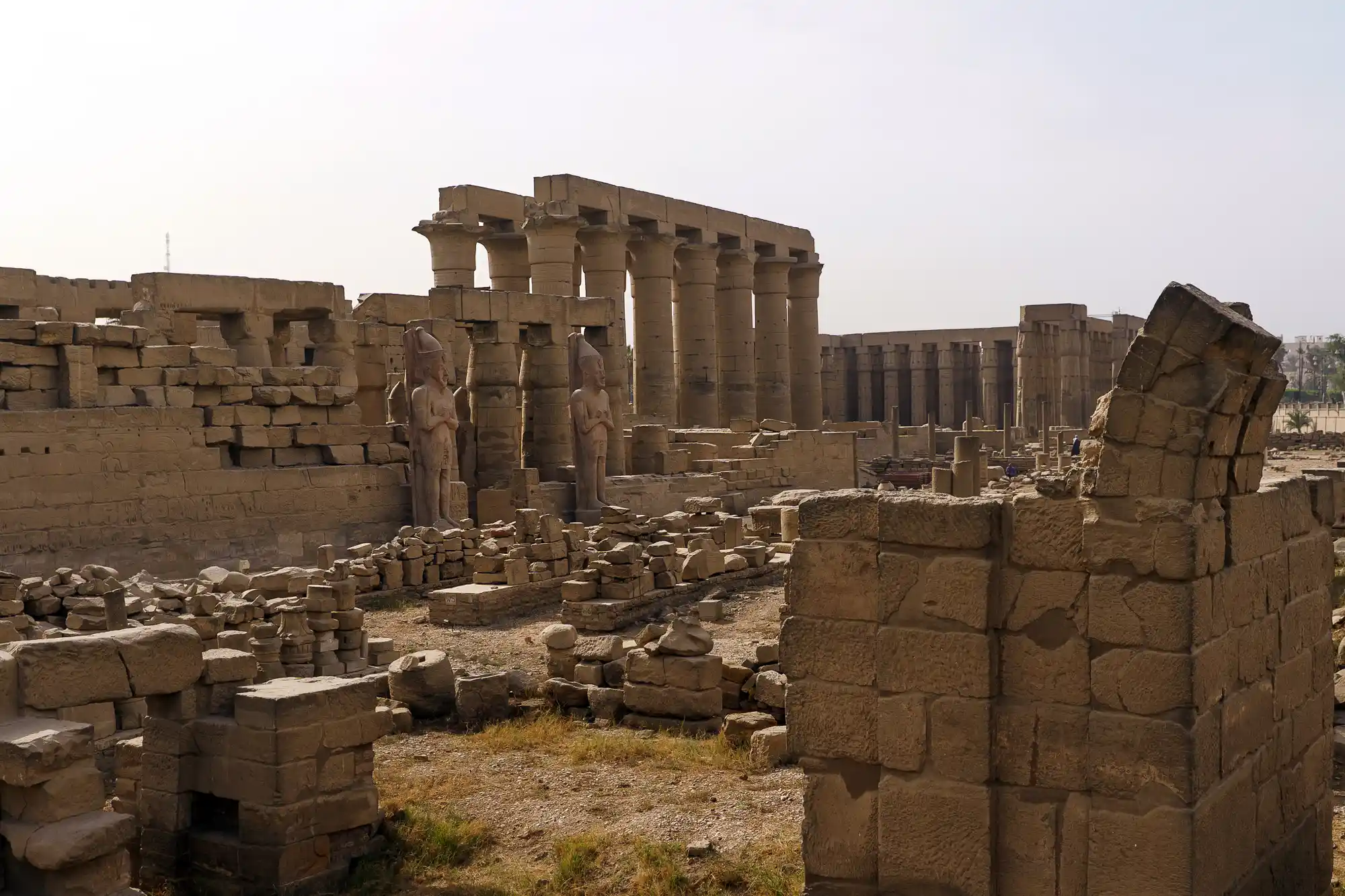 Two standing pharaoh statues framed by massive sandstone blocks at Luxor Temple, in soft overhead light.