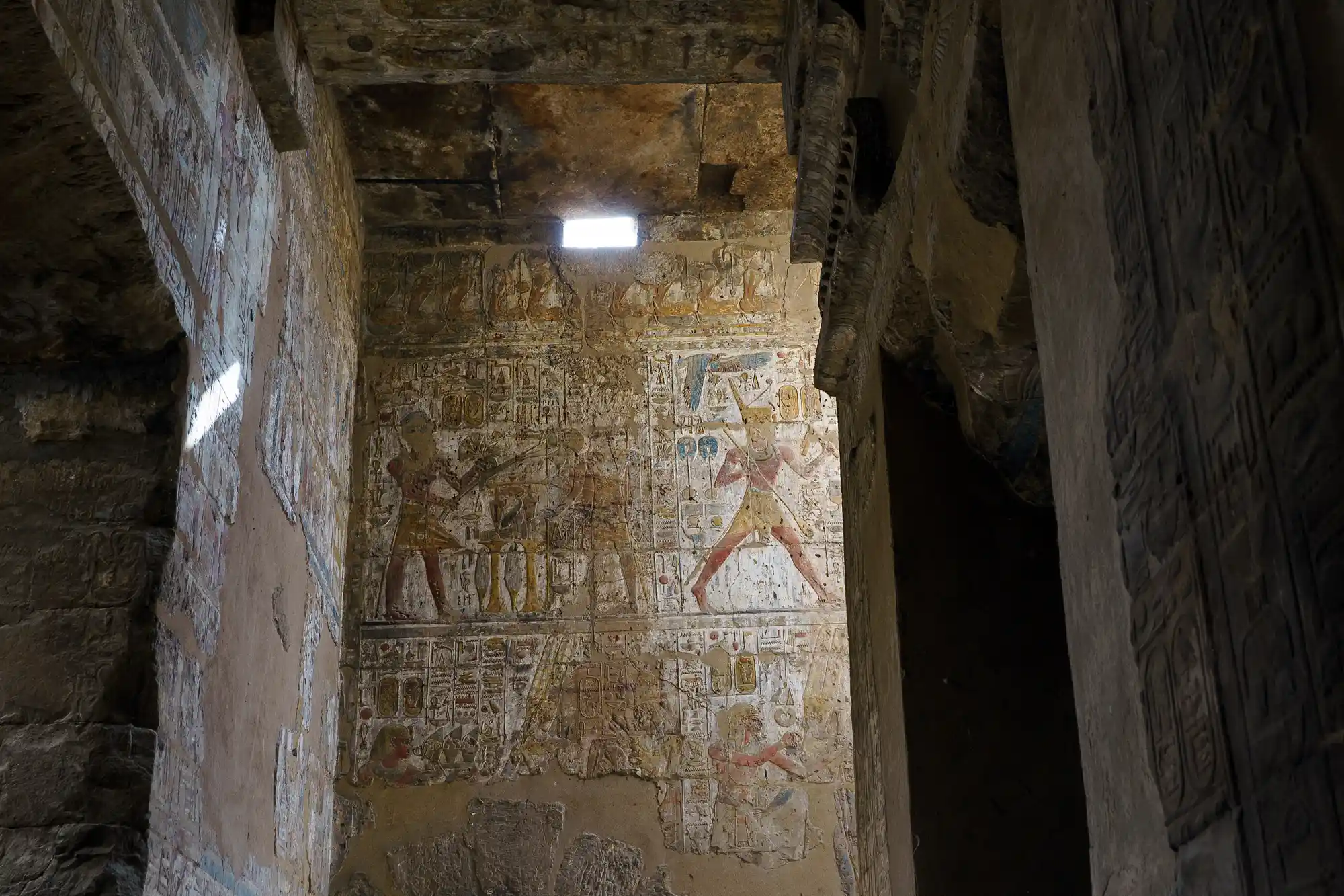 Relief figures in faded ochre and blue pigment on a carved wall inside Luxor Temple, lit from above.
