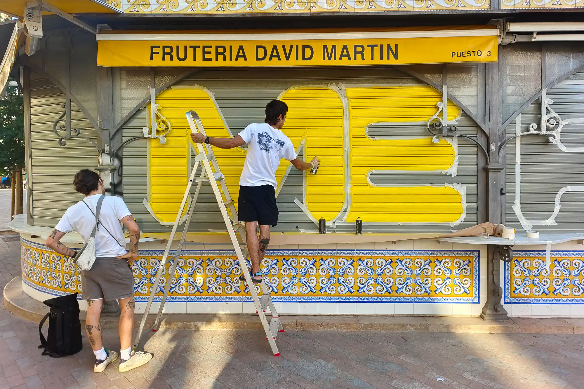 Street art at Fruteria David Martin man standing on a latter spraying ME