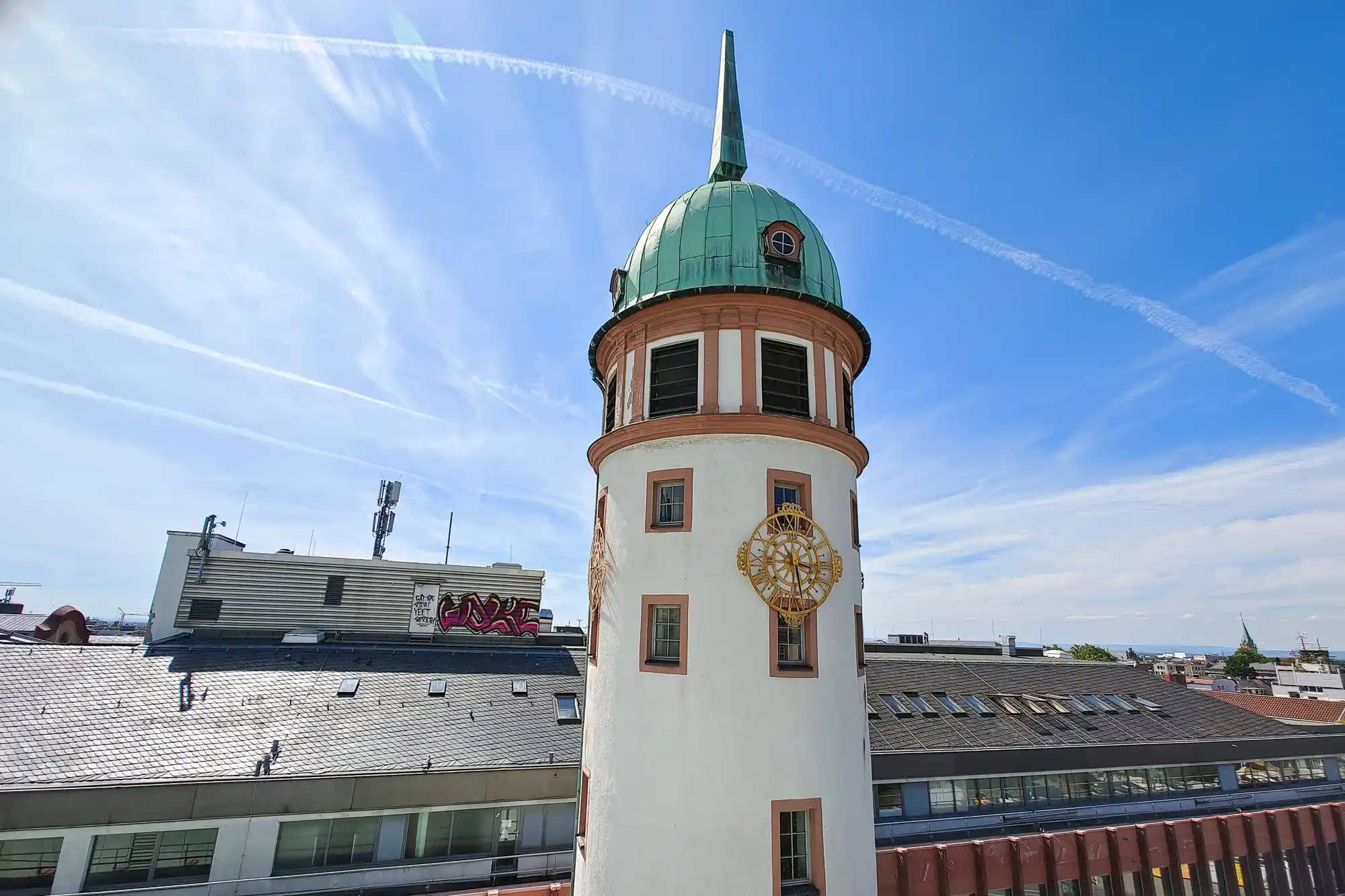 Close-up of Darmstadt's Weisser Turm with its green dome and gold clock face, the smooth white walls lit by bright sunlight.