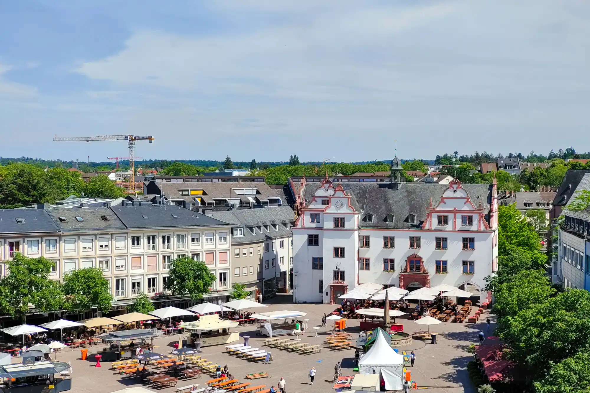 Darmstadt's Marktplatz seen from the Henschel terrace, with white buildings with red trim and people at tables beneath white umbrellas.
