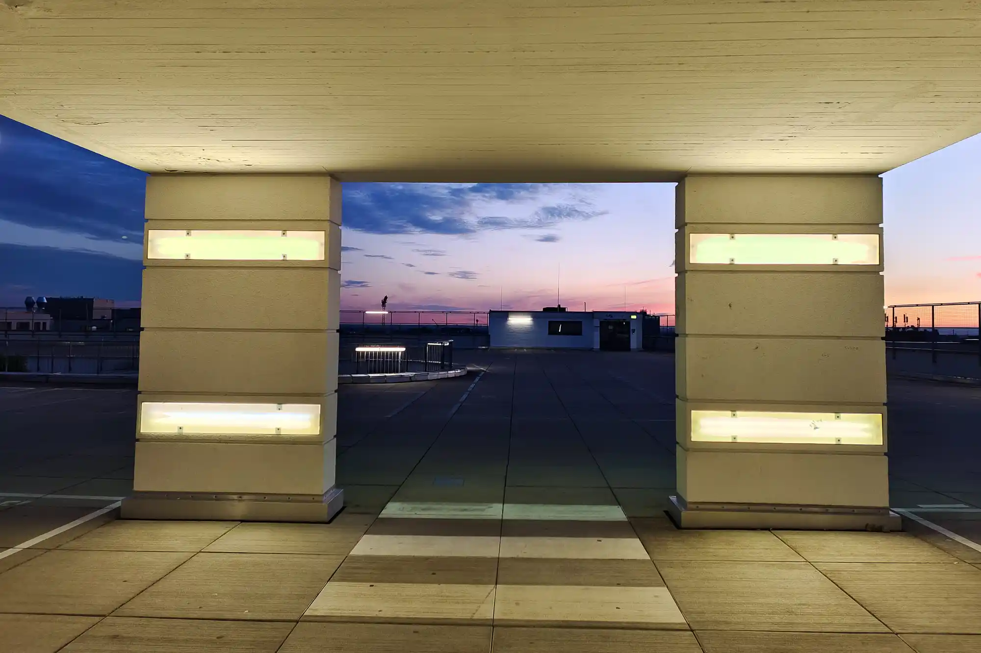 Concrete pillars with glowing rectangular lights on top of a parking garage in Darmstadt, under a pink and blue evening sky.