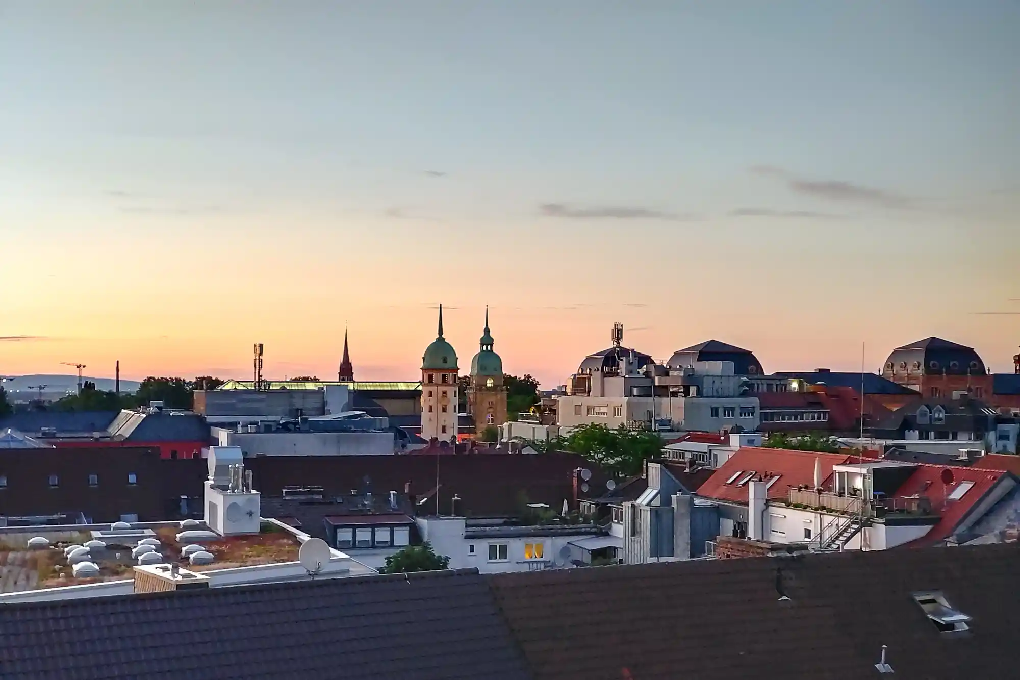 Red and dark tiled rooftops of Darmstadt in orange evening light, with two towers topped by green domes rising above.