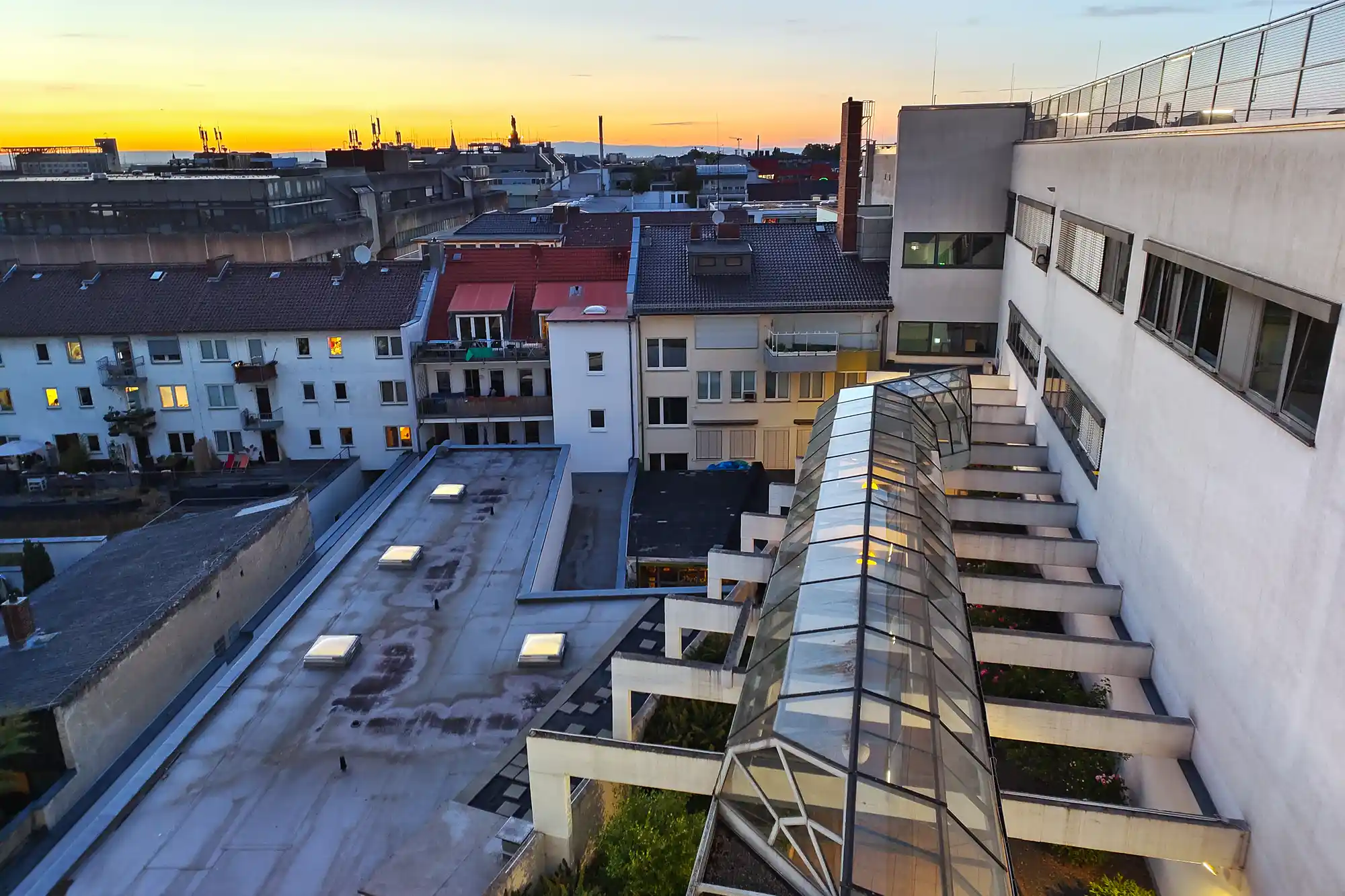 Darmstadt rooftops with a glass walkway and flat concrete surfaces, with warm yellow light glowing in the evening sky.