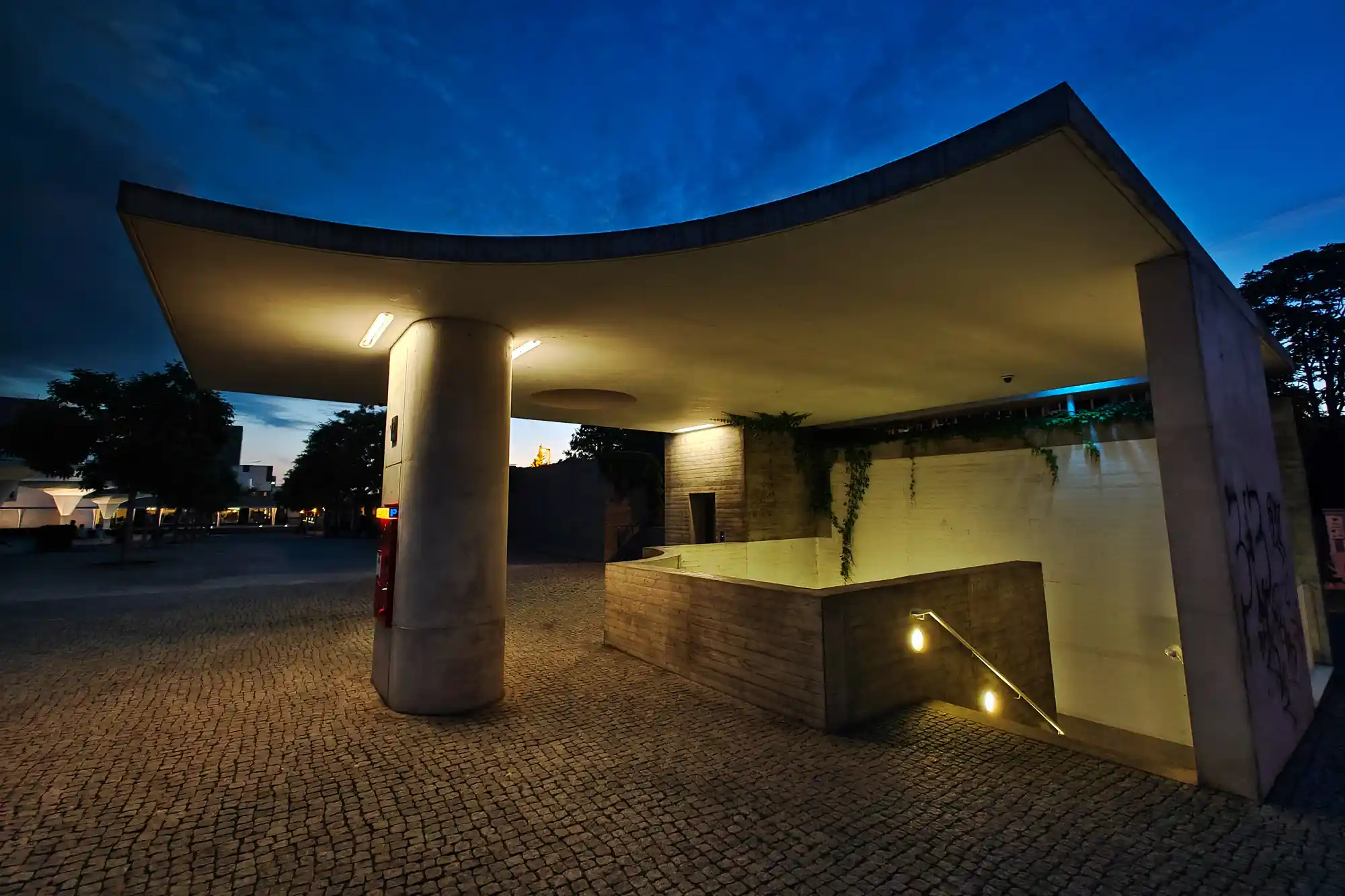 A curved concrete structure with warm lights above a cobblestone square in Darmstadt under a dark blue night sky.