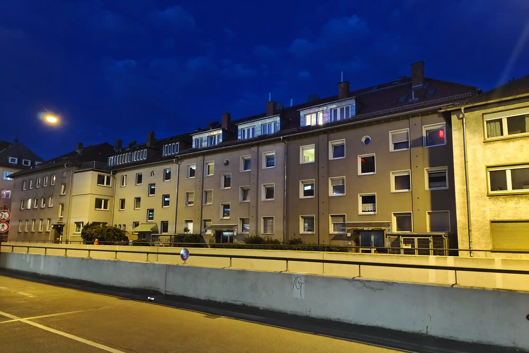 Darmstadt buildings lit by yellow light under a deep blue sky, with faint markings on a concrete barrier in front.
