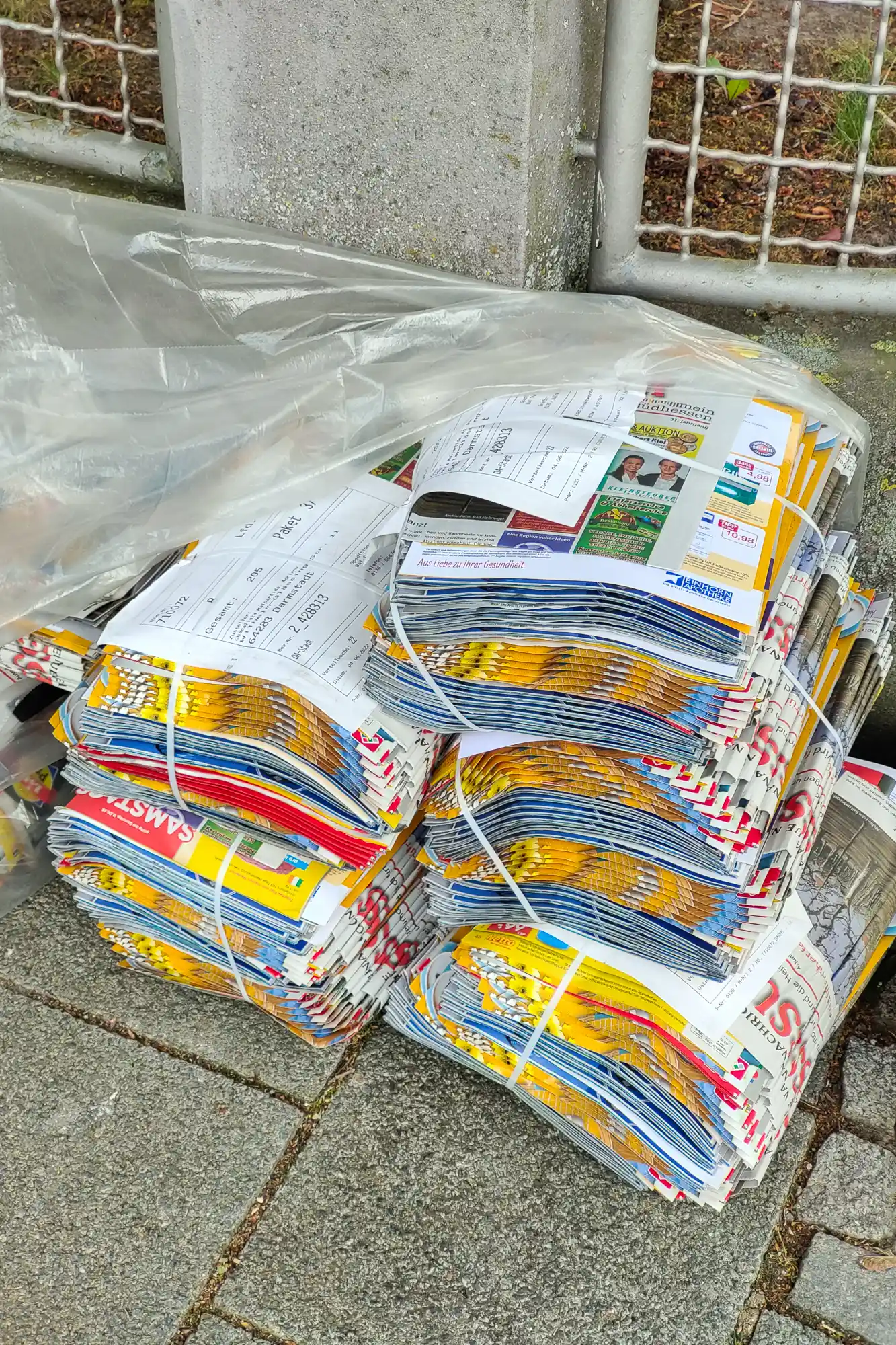 Bundles of German advertising leaflets (Werbeprospekte) tied with white string under clear plastic on grey stone in Darmstadt.