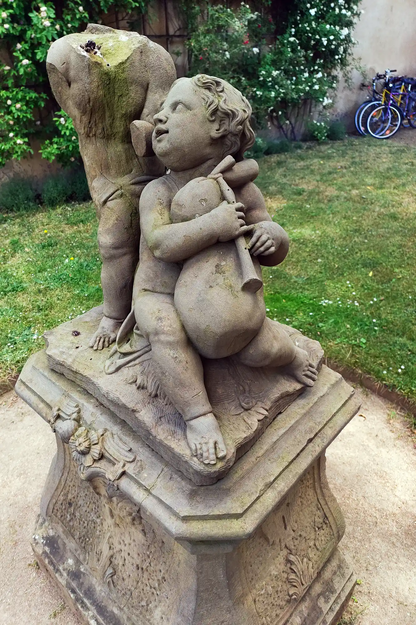 A stone statue of a child holding a bag in Darmstadt, seen from a low angle with green moss growing on the stone.