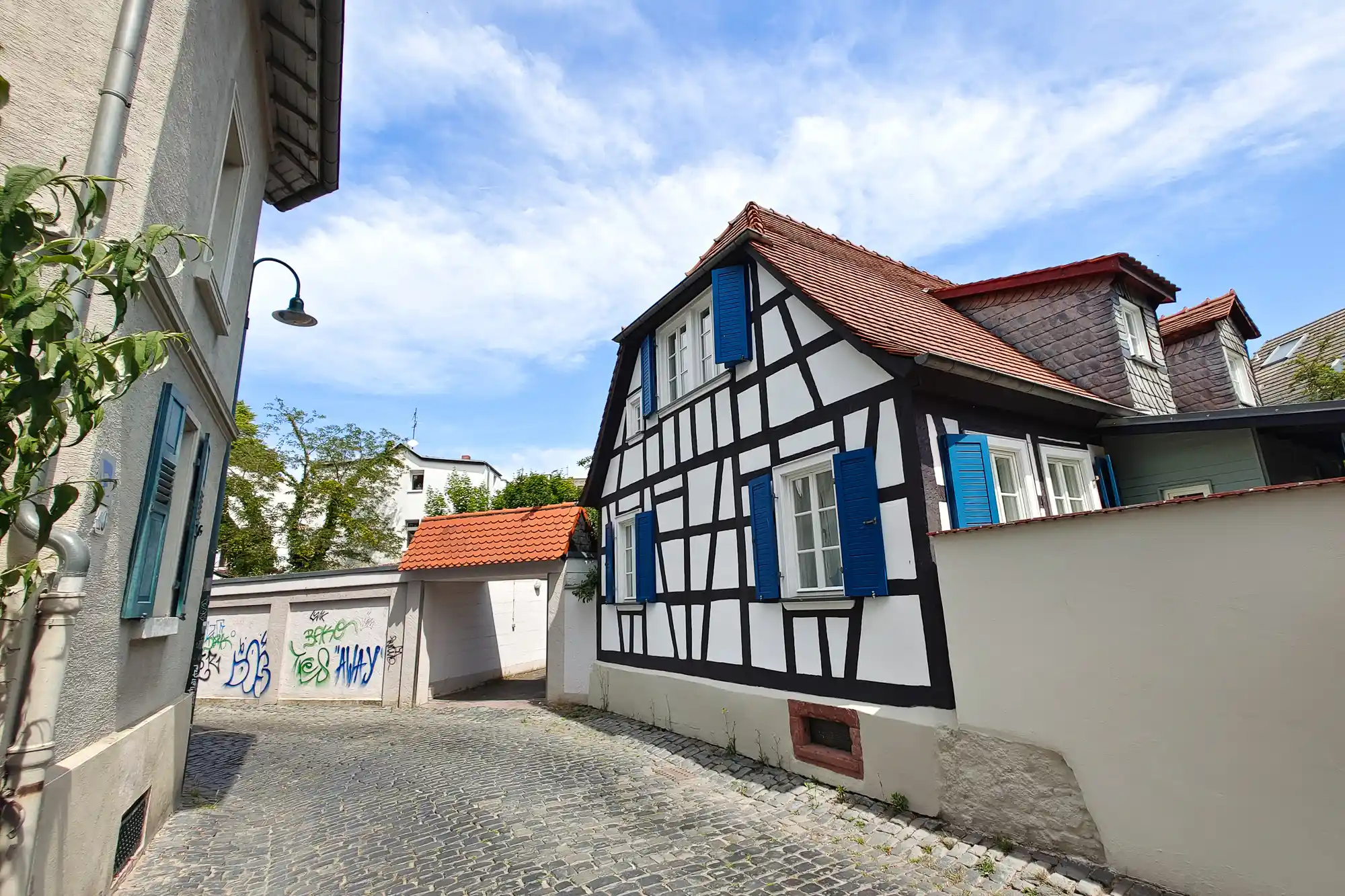 A black-and-white half-timbered house with blue shutters on a cobblestone lane in Darmstadt, in bright light.