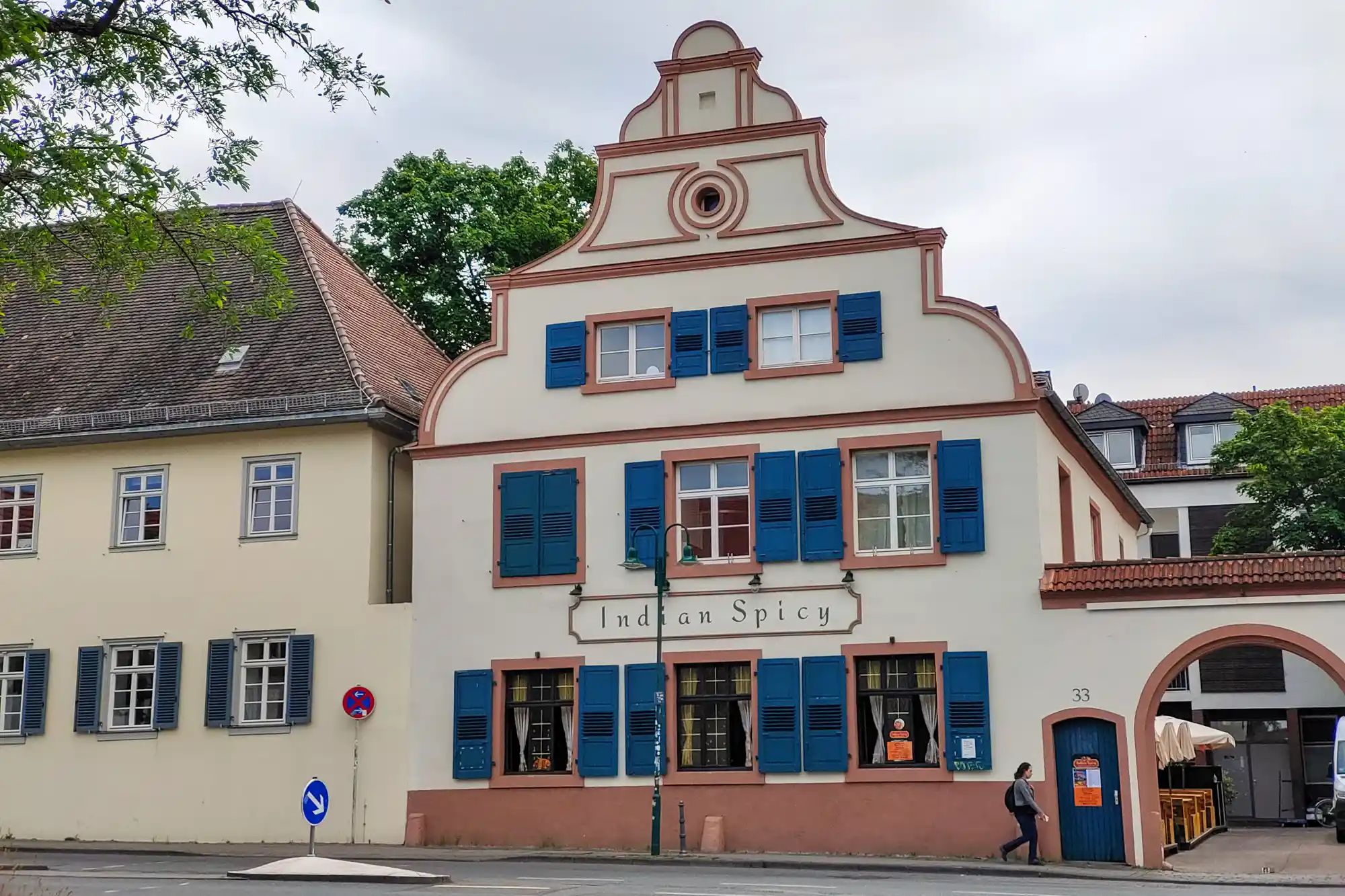 A cream building with blue shutters and pink trim in Darmstadt, with a person walking past a blue door under overcast light.