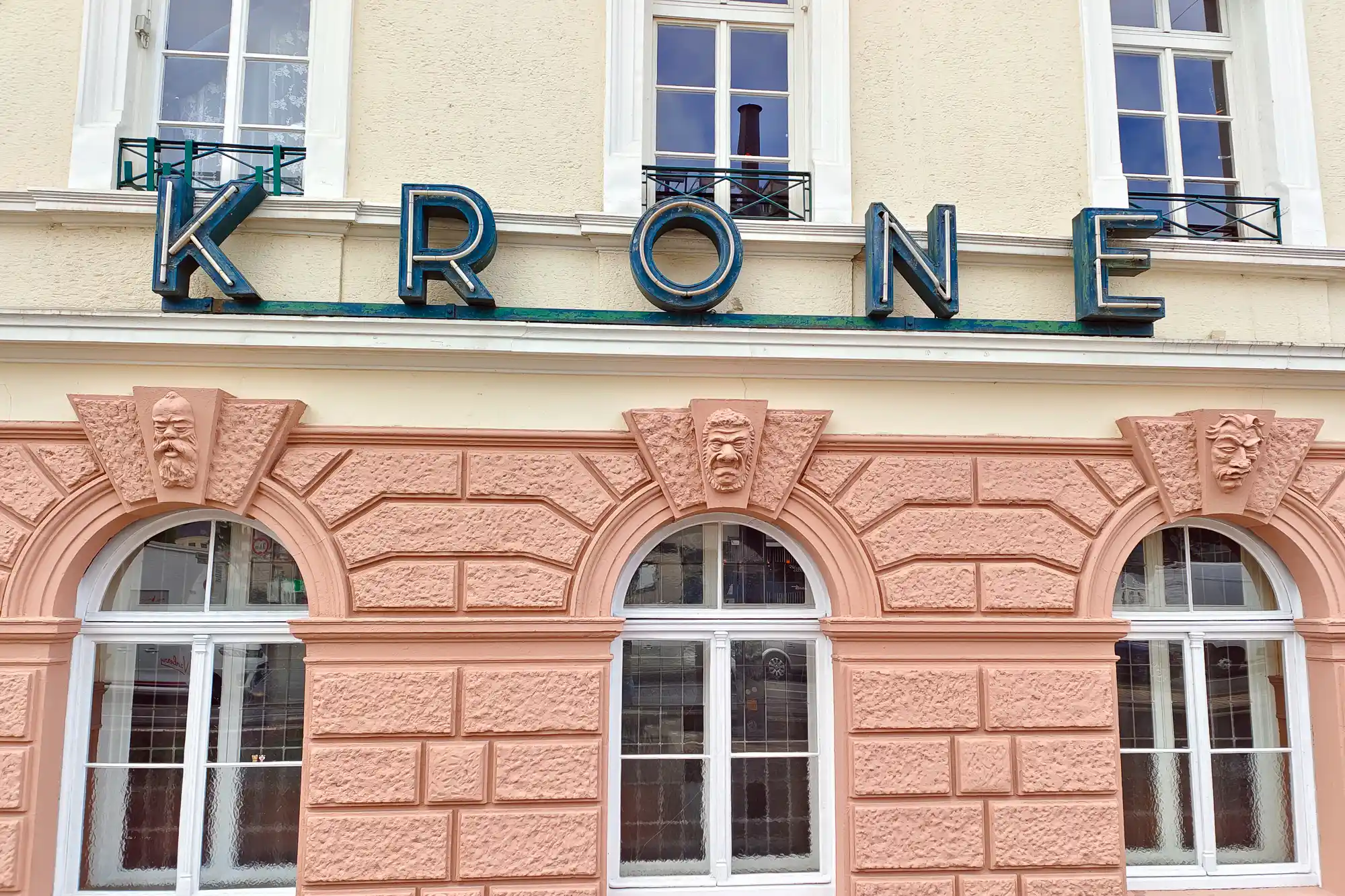 Blue lettering above three arched windows in pink stone in Darmstadt, with a carved face above each arch.