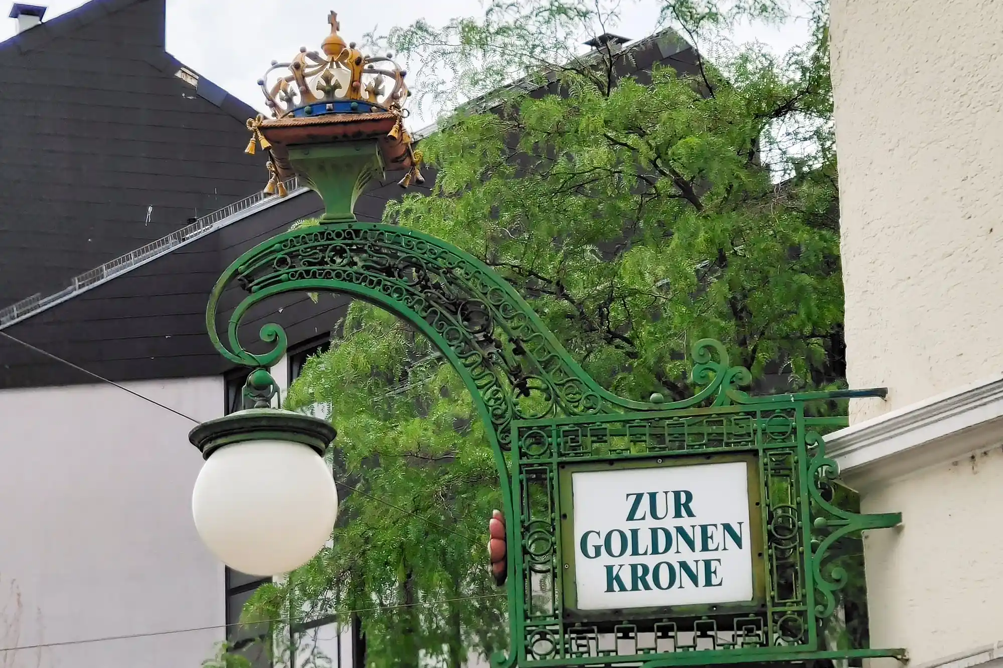 A green metal sign with a gold crown and a white globe lamp in Darmstadt, set against a background of green foliage.