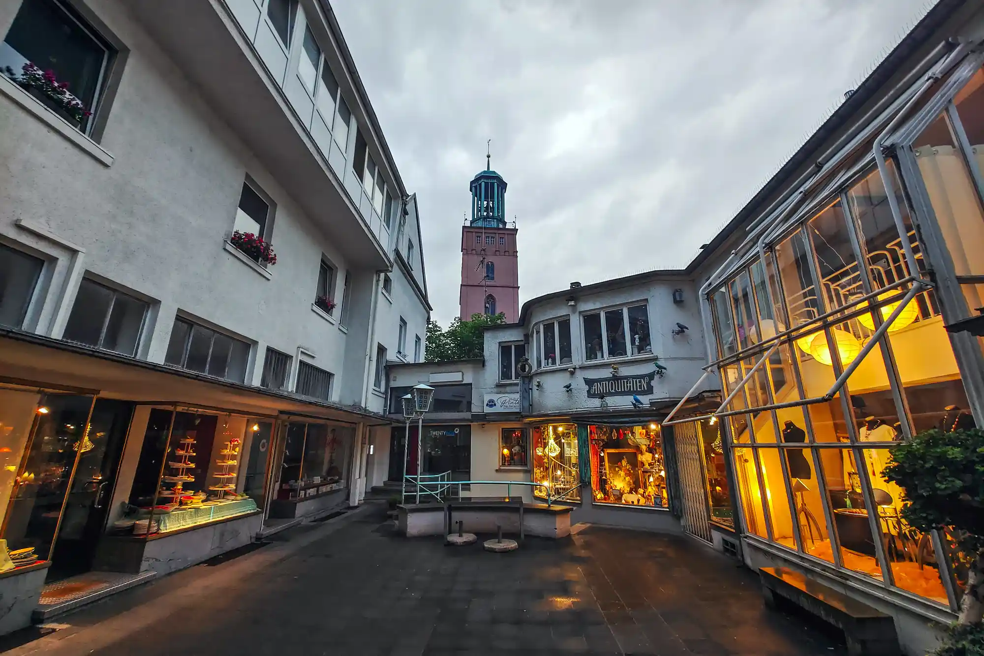 A narrow stone path leading to a pink tower in Darmstadt under a grey evening sky, with warm light glowing from glass windows.