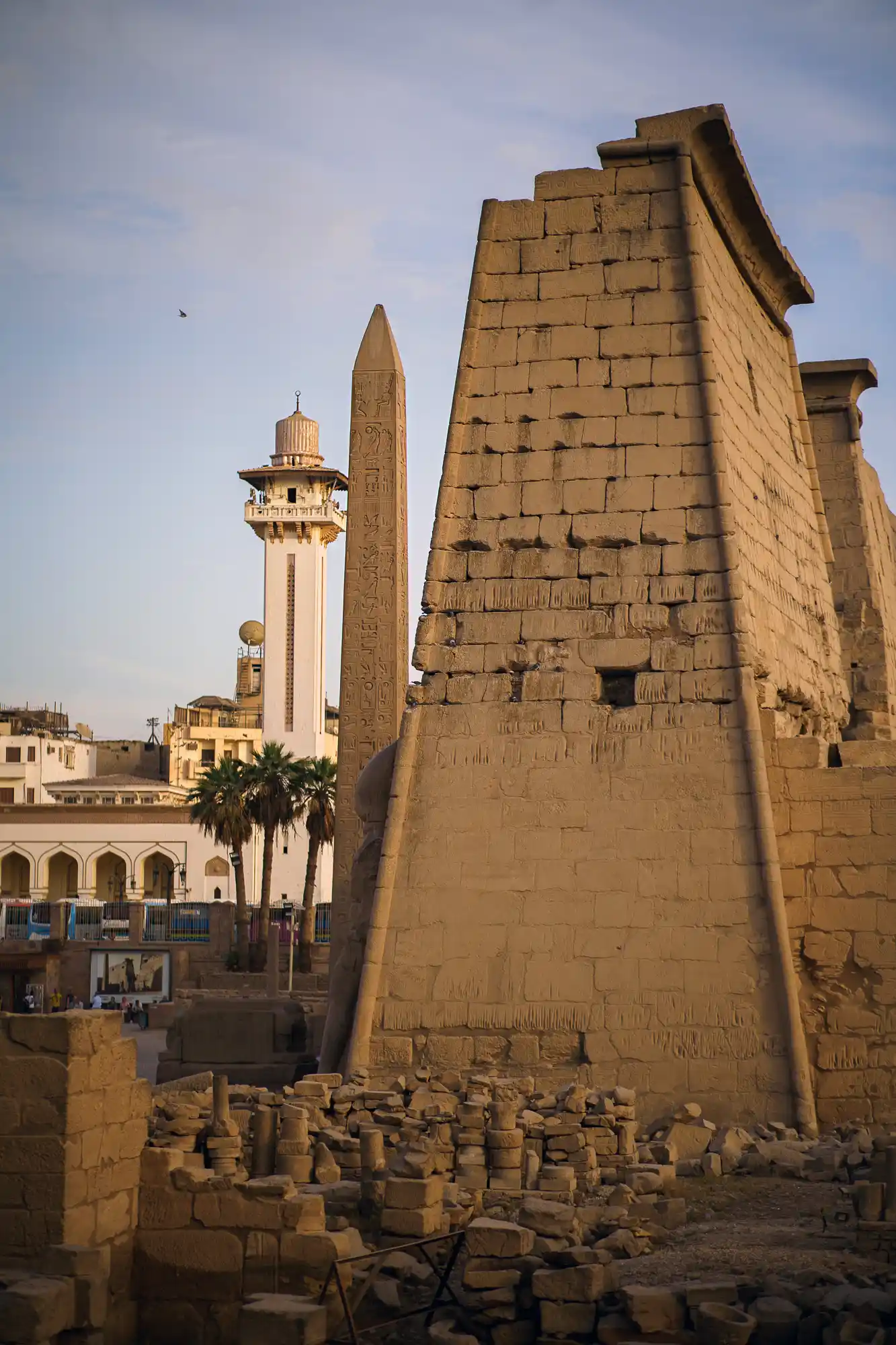 The carved obelisk at the Luxor Temple entrance gate in warm light, with a white tower rising behind it.