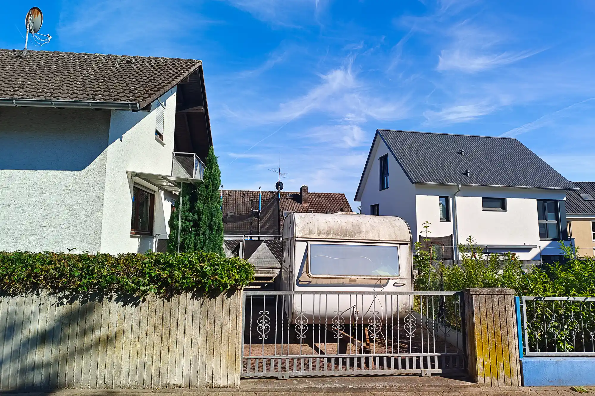 A grey trailer behind a metal gate with scrollwork in Traisa, next to a wooden fence and green bushes.