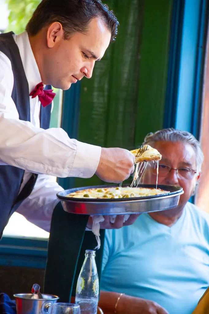 Pizzeria Banchero waiter serving cheesy pizza